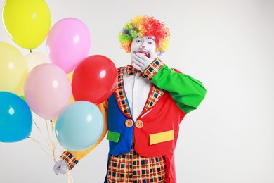 Photo of Emotional clown with colorful balloons on light background