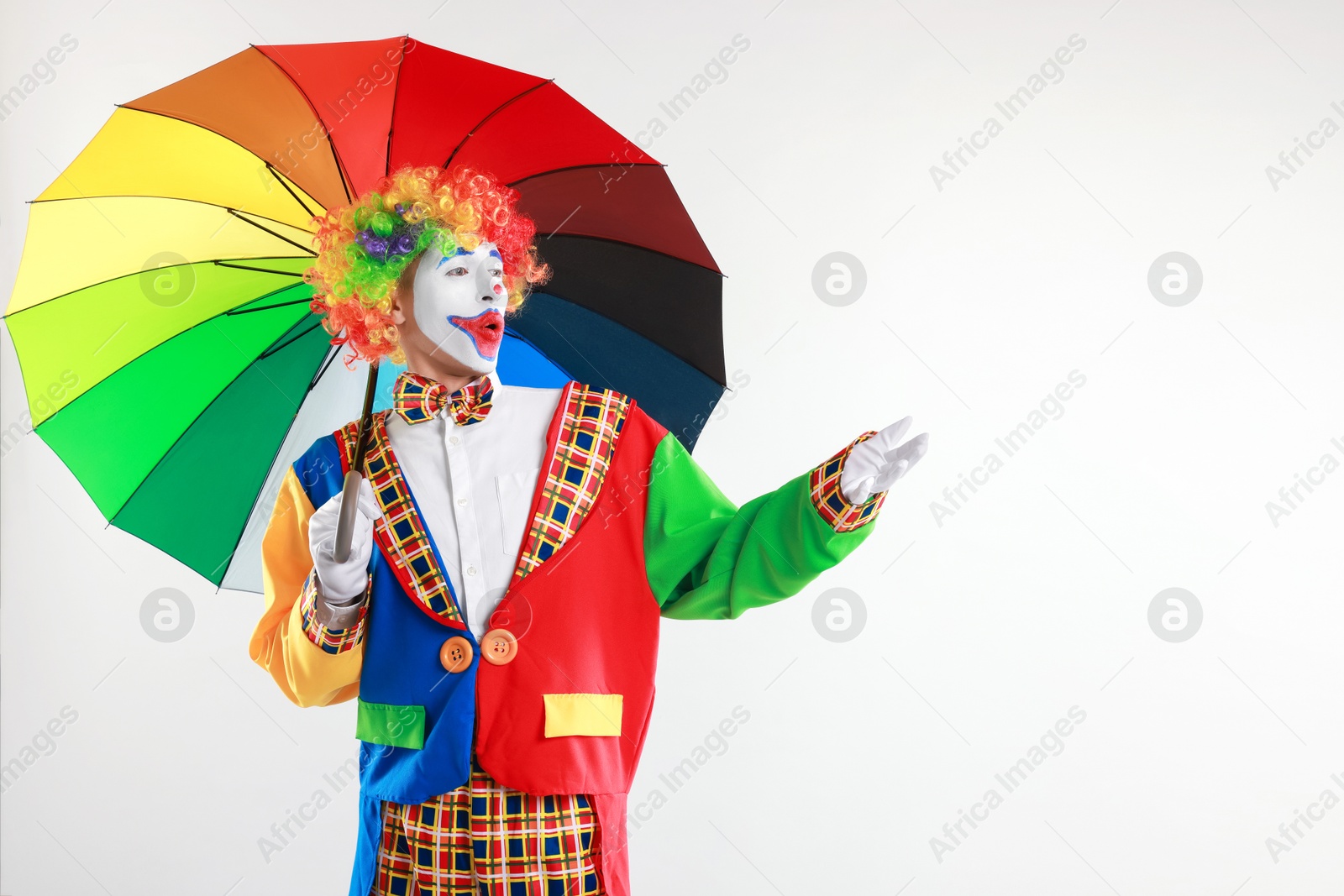 Photo of Emotional clown with colorful umbrella on light background, space for text