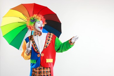 Photo of Emotional clown with colorful umbrella on light background, space for text