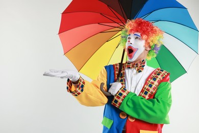 Photo of Emotional clown with colorful umbrella on light background