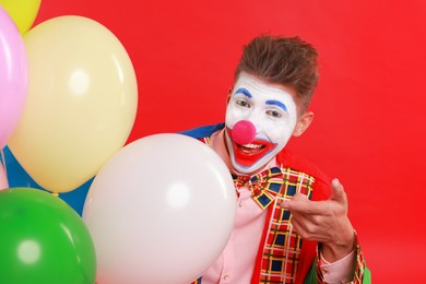 Photo of Happy clown with colorful balloons on red background