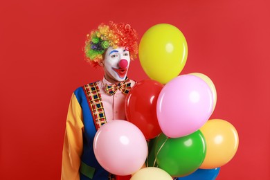 Photo of Emotional clown with colorful balloons on red background