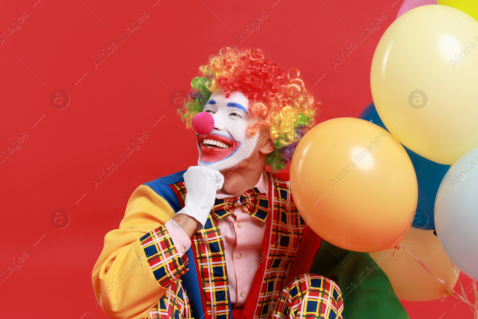 Photo of Happy clown with colorful balloons on red background