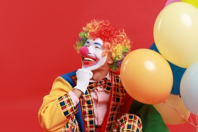 Photo of Happy clown with colorful balloons on red background