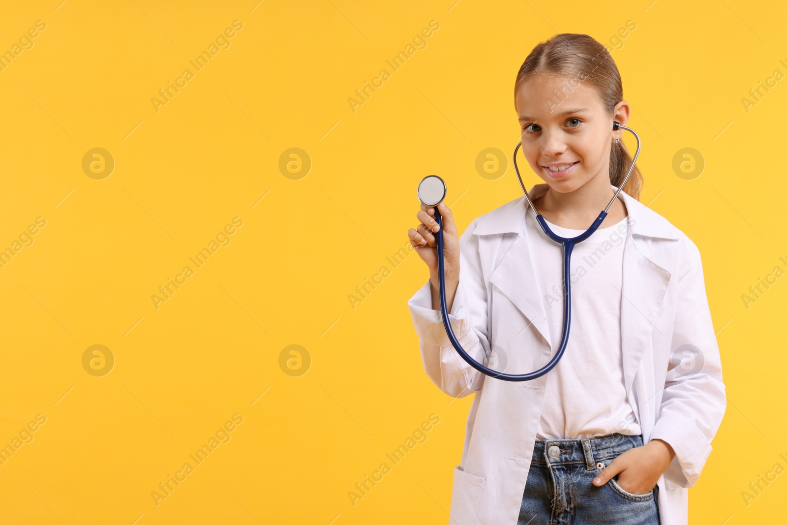 Photo of Girl with stethoscope pretending to be doctor on yellow background, space for text. Dreaming of future profession