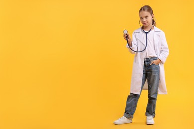 Photo of Girl with stethoscope pretending to be doctor on yellow background, space for text. Dreaming of future profession