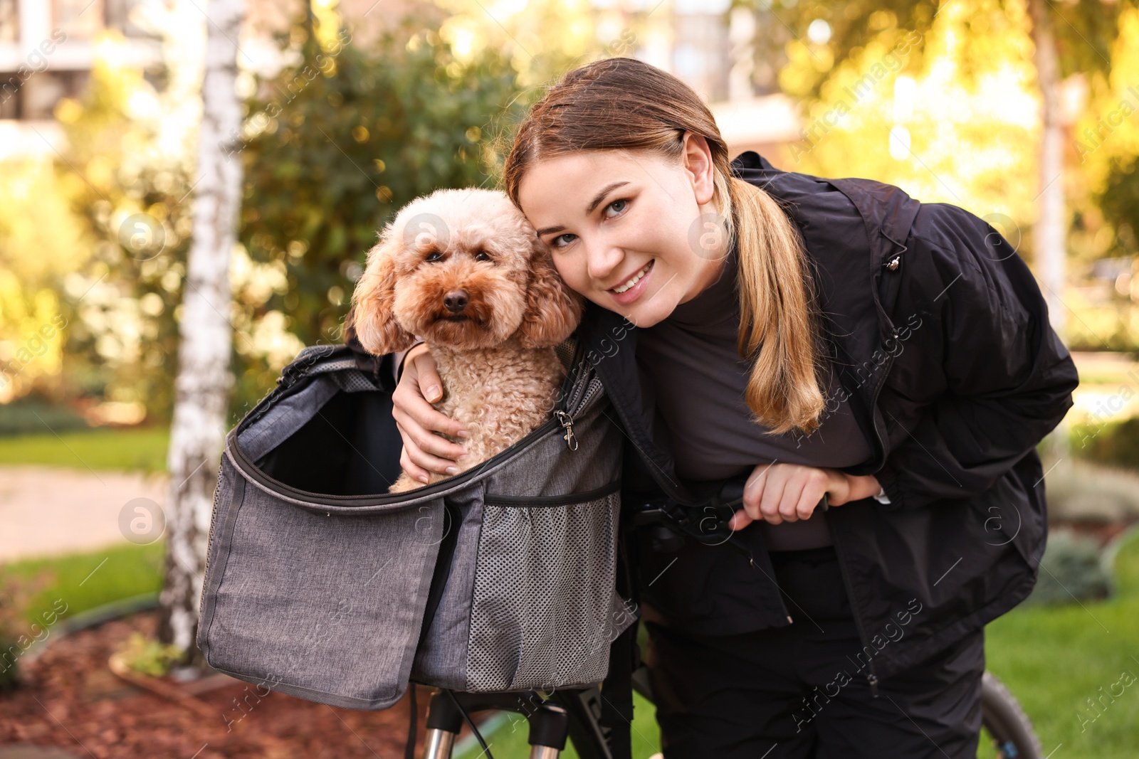 Photo of Woman with bicycle and cute Toy Poodle dog in pet carrier outdoors