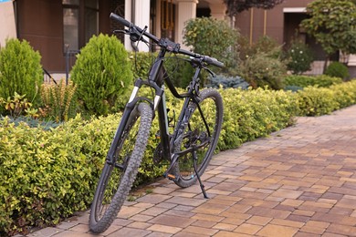 Photo of Black modern bicycle parked near green plants outdoors