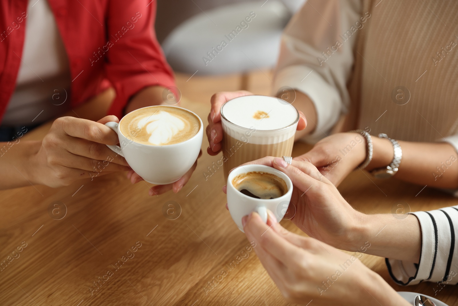 Photo of Women with cups of delicious coffee drinks at wooden table in cafe, closeup