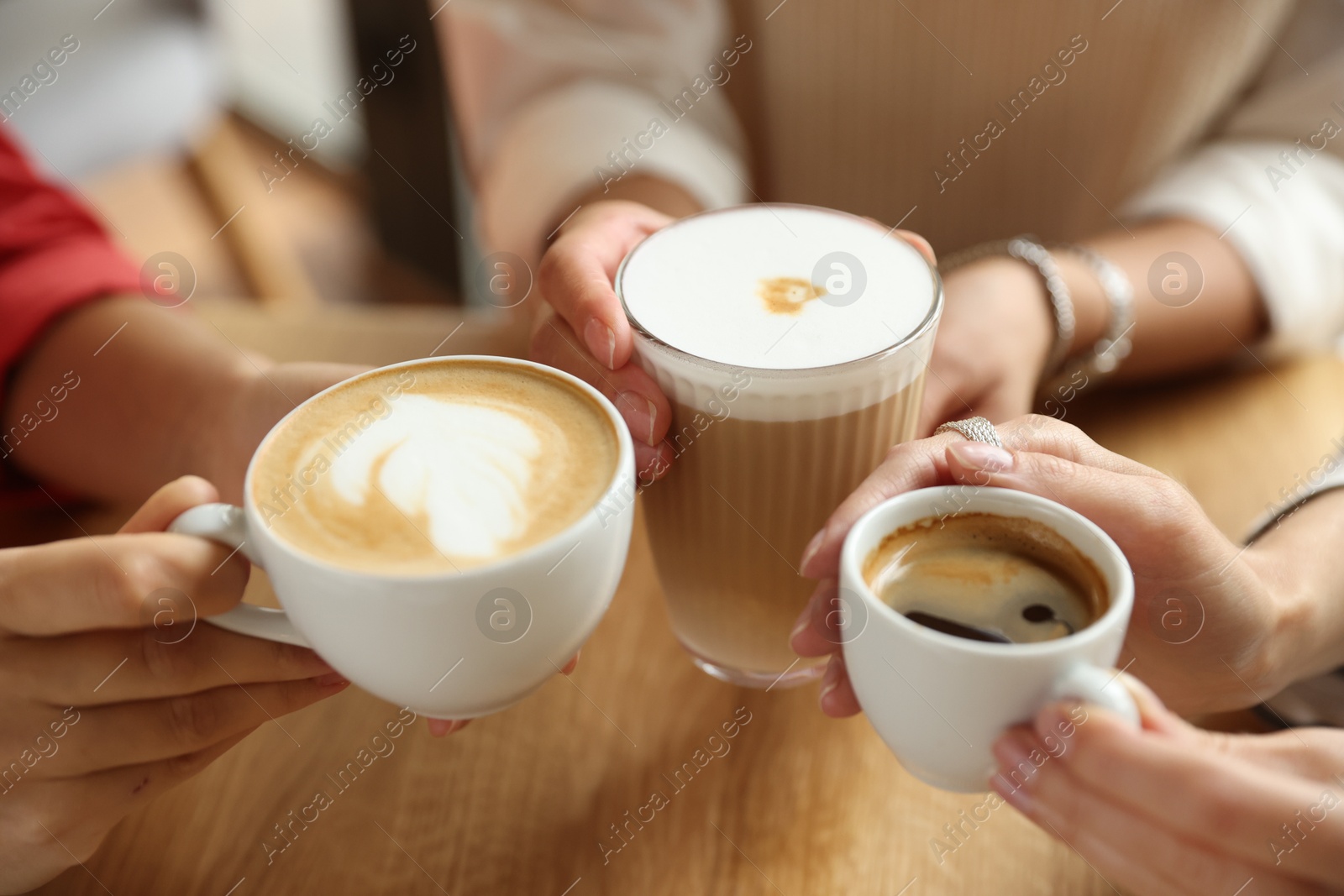 Photo of Women with cups of delicious coffee drinks at wooden table in cafe, closeup