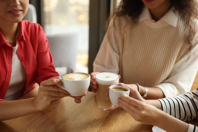 Photo of Women with cups of delicious coffee drinks at wooden table in cafe, closeup