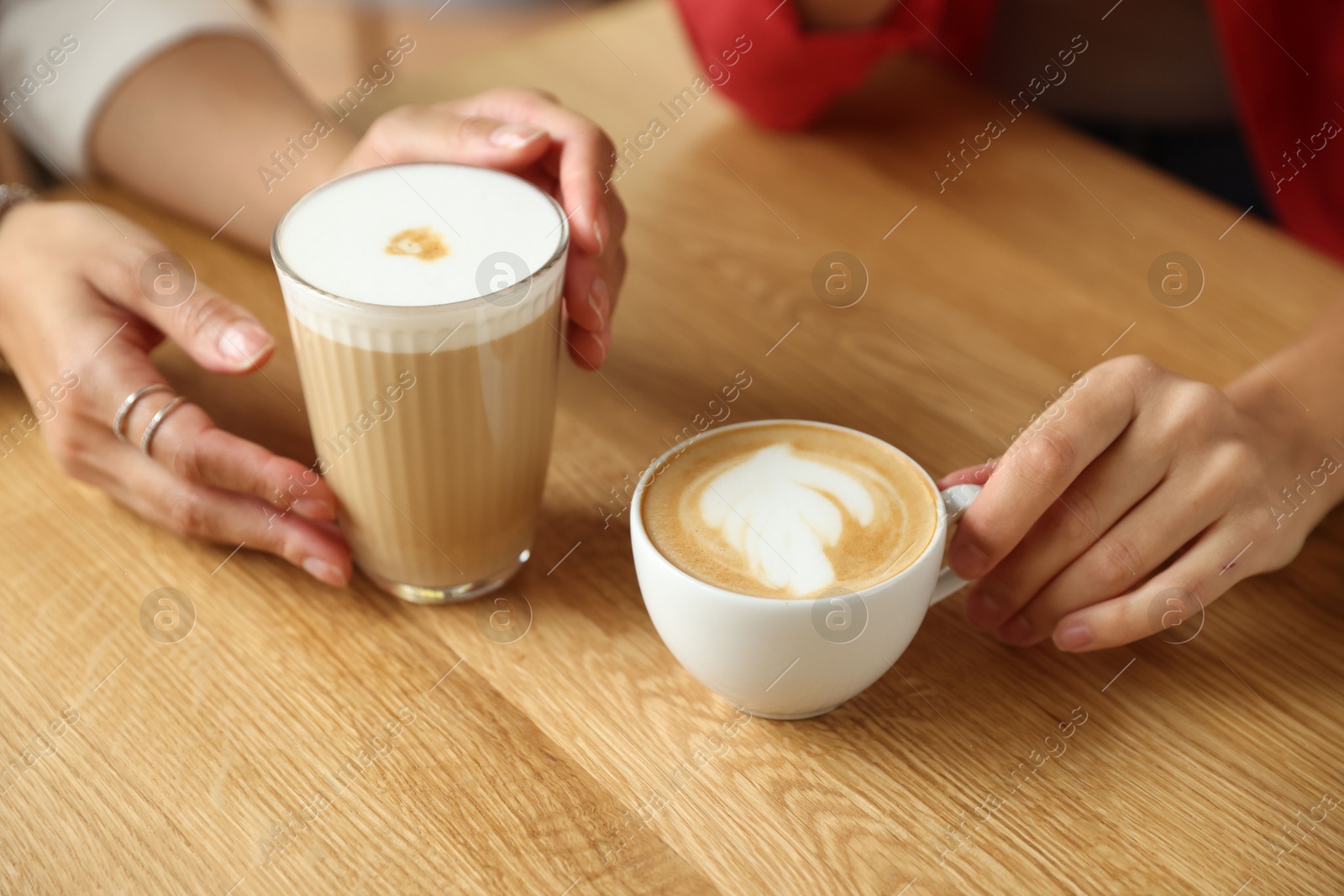 Photo of Women with cups of delicious coffee drinks at wooden table in cafe, closeup