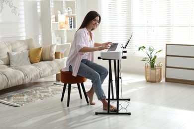 Photo of Smiling woman playing synthesizer at home. Electronic musical instrument