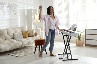 Photo of Smiling woman playing synthesizer and dancing at home