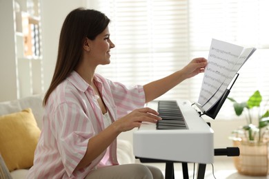 Photo of Smiling woman playing synthesizer at home. Electronic musical instrument