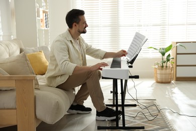 Photo of Bearded man playing synthesizer at home. Electronic musical instrument