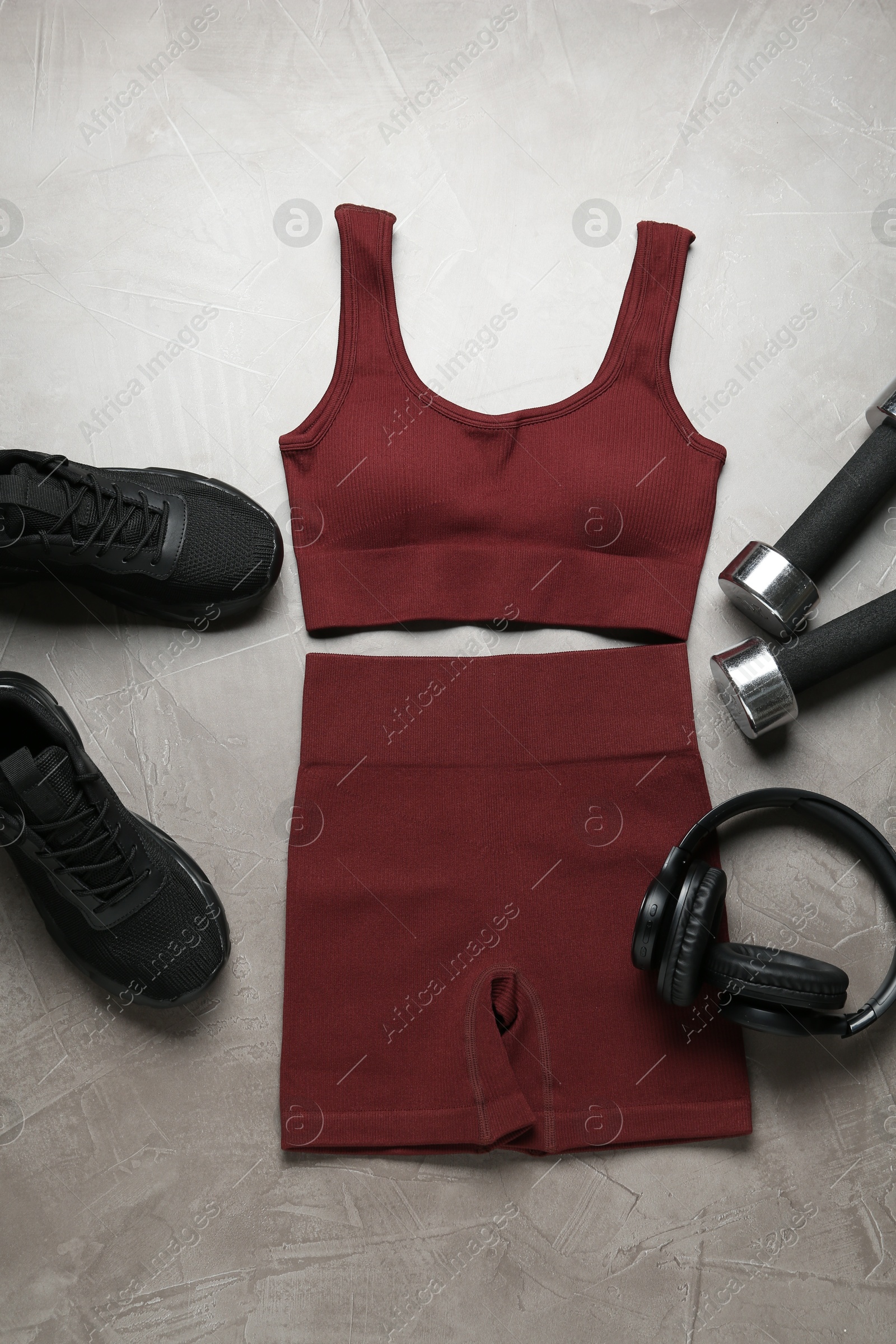 Photo of Brown sportswear, black sneakers, dumbbells and headphones on gray textured background, flat lay