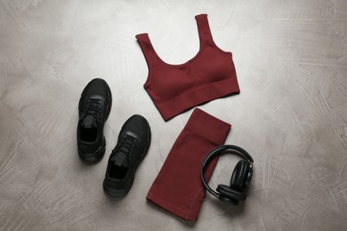 Photo of Brown sportswear, black sneakers and headphones on gray textured background, flat lay