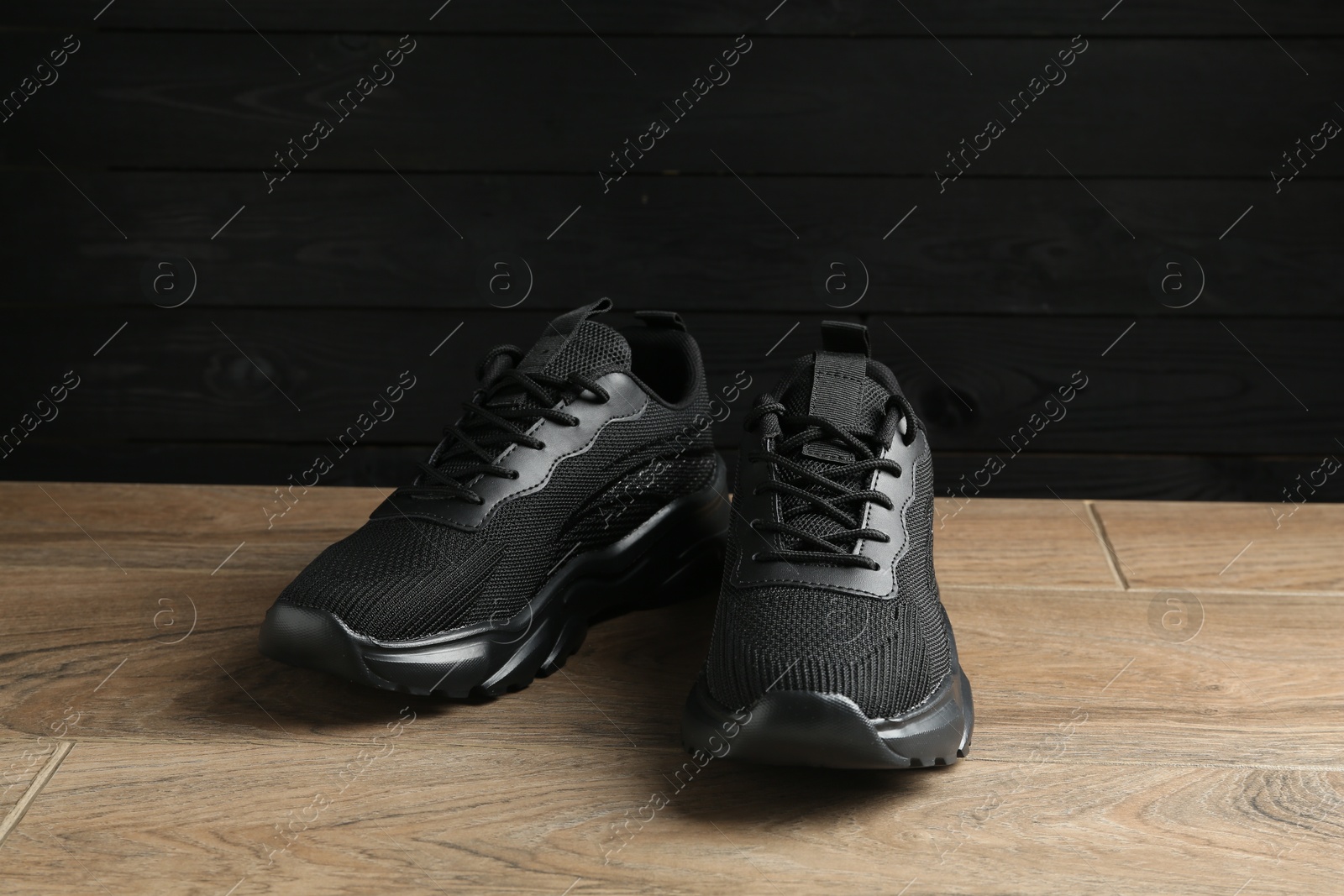 Photo of Pair of stylish black sneakers on floor against dark wooden background