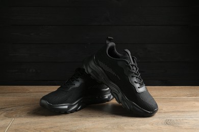 Photo of Pair of stylish black sneakers on floor against dark wooden background