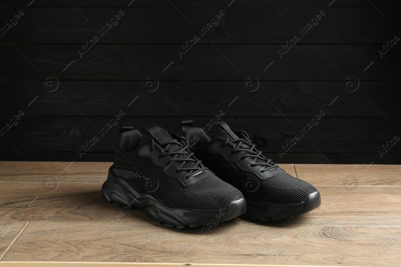 Photo of Pair of stylish black sneakers on floor against dark wooden background