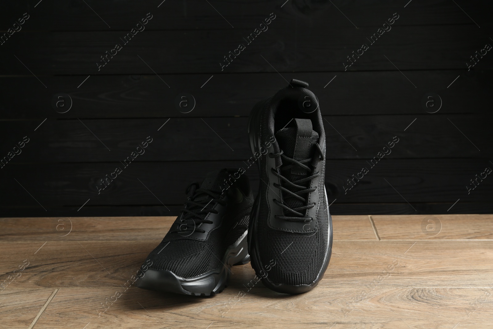 Photo of Pair of stylish black sneakers on floor against dark wooden background