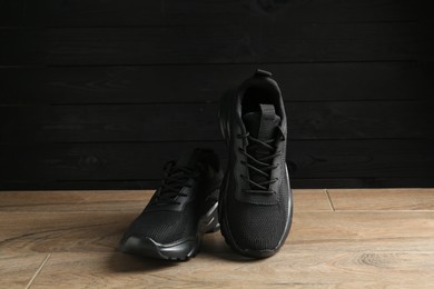 Photo of Pair of stylish black sneakers on floor against dark wooden background