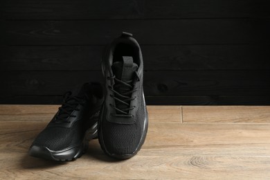 Photo of Pair of stylish black sneakers on floor against dark wooden background, space for text