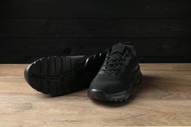 Photo of Pair of stylish black sneakers on floor against dark wooden background