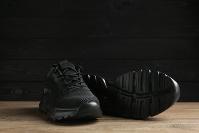 Photo of Pair of stylish black sneakers on floor against dark wooden background