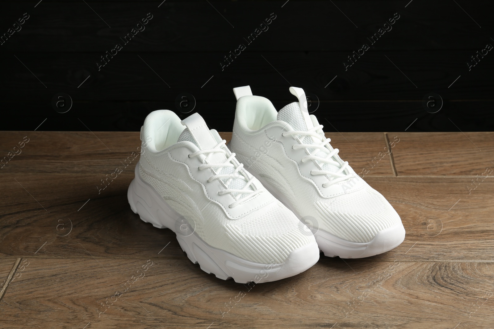 Photo of Pair of stylish white sneakers on floor against dark background