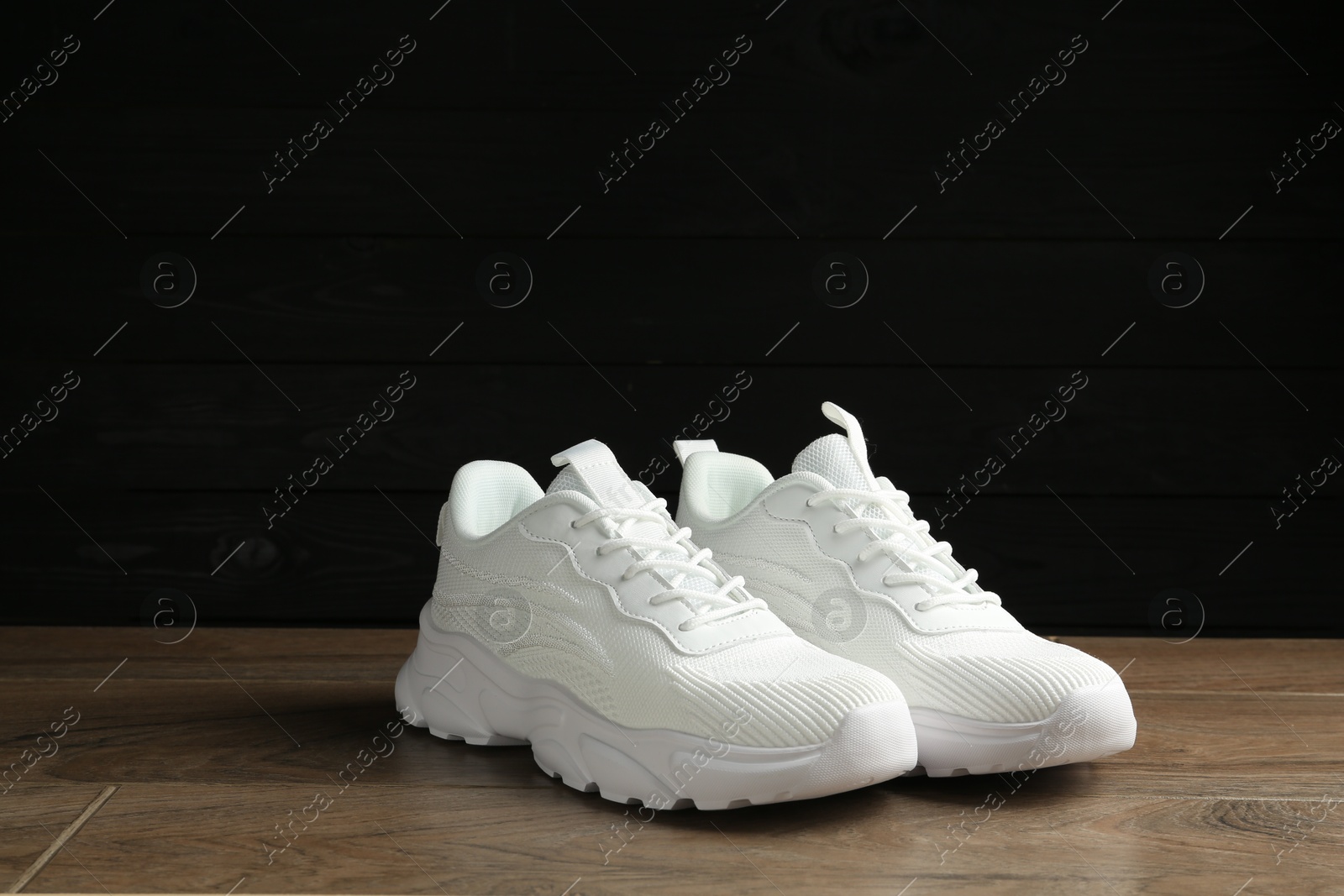 Photo of Pair of stylish white sneakers on floor against dark background