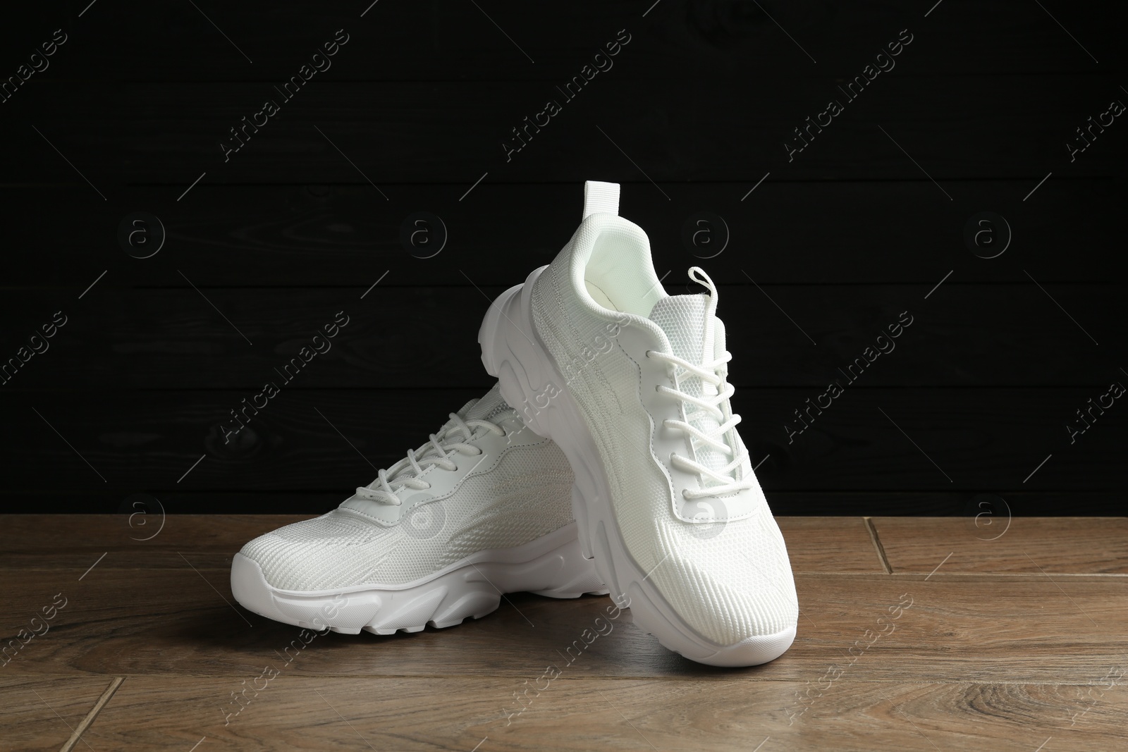 Photo of Pair of stylish white sneakers on floor against dark background