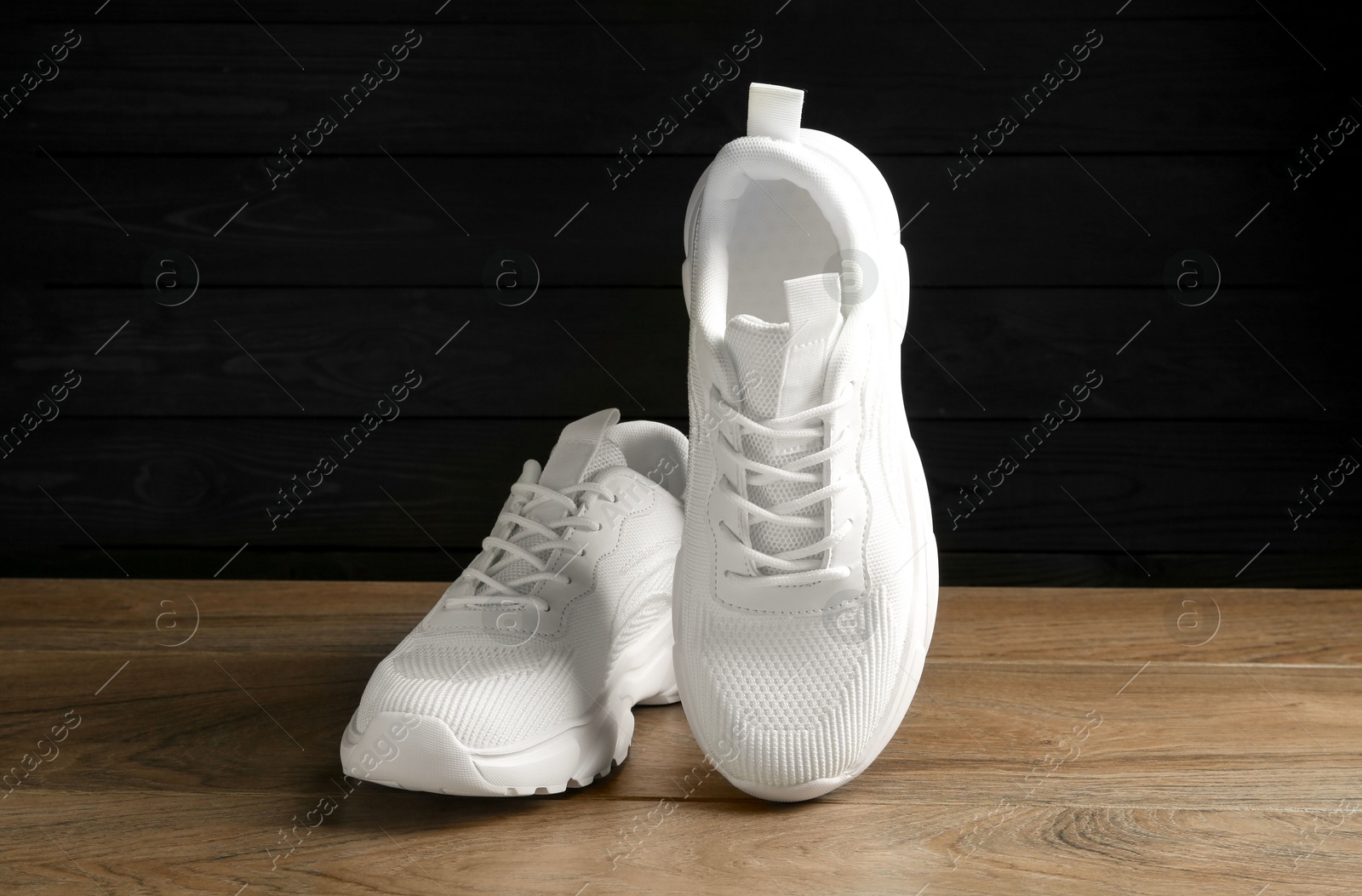 Photo of Pair of stylish white sneakers on floor against dark background