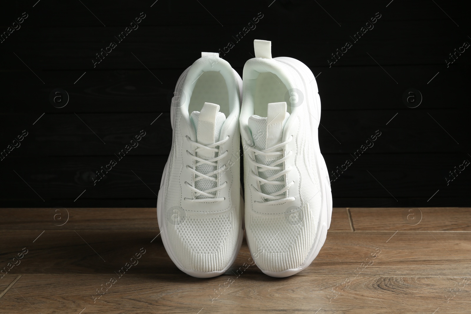 Photo of Pair of stylish white sneakers in air on floor against dark background