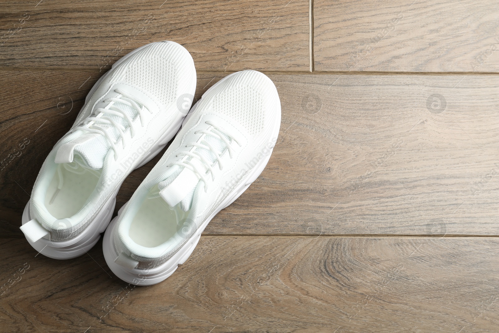 Photo of Pair of stylish white sneakers on wooden background, top view. Space for text