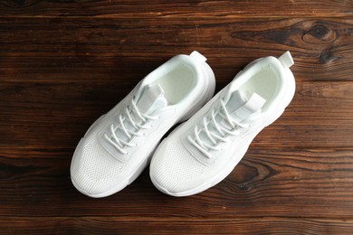 Photo of Pair of stylish white sneakers on wooden background, top view