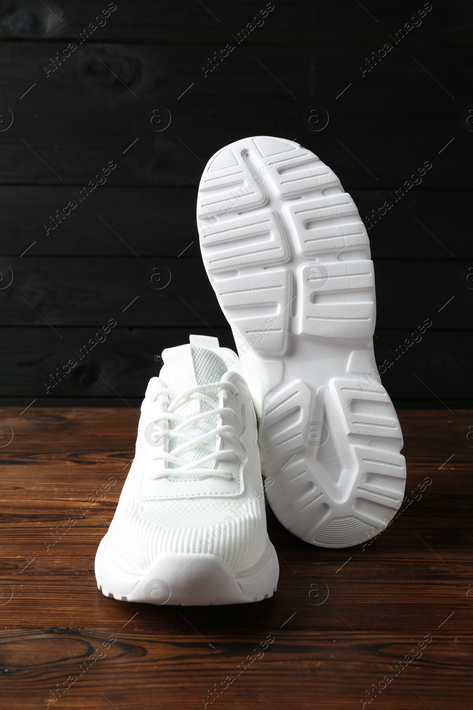 Photo of Pair of stylish white sneakers on floor against dark wooden background