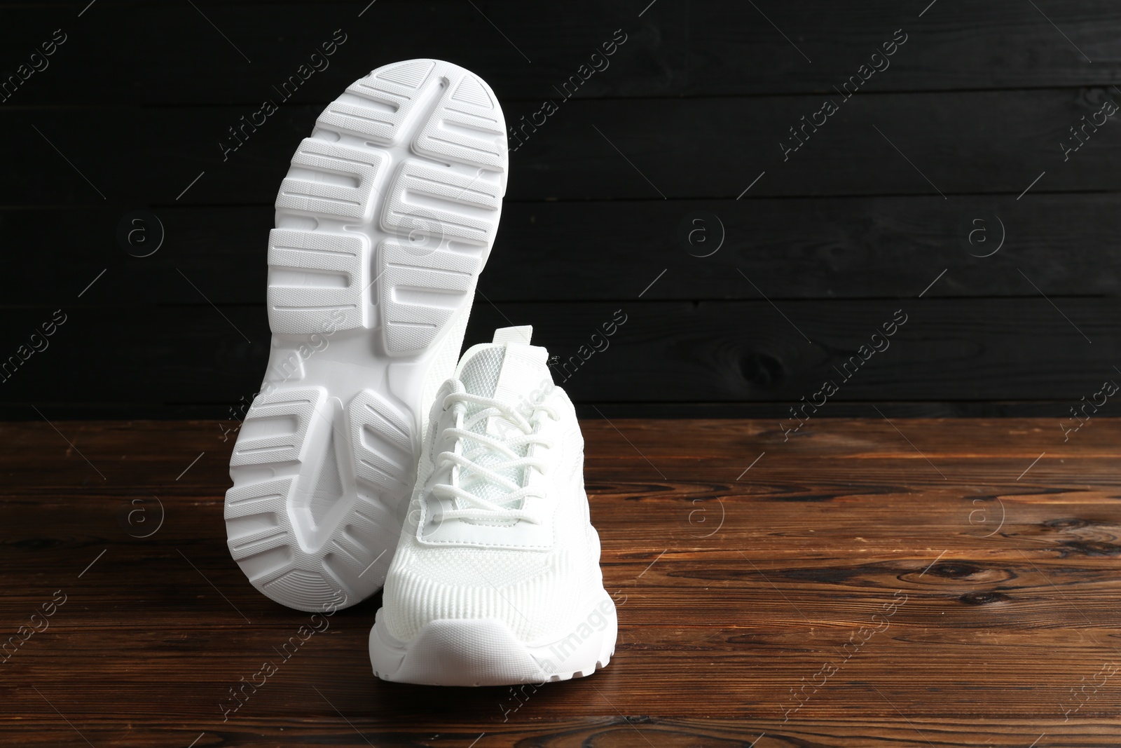 Photo of Pair of stylish white sneakers on floor against dark wooden background, space for text