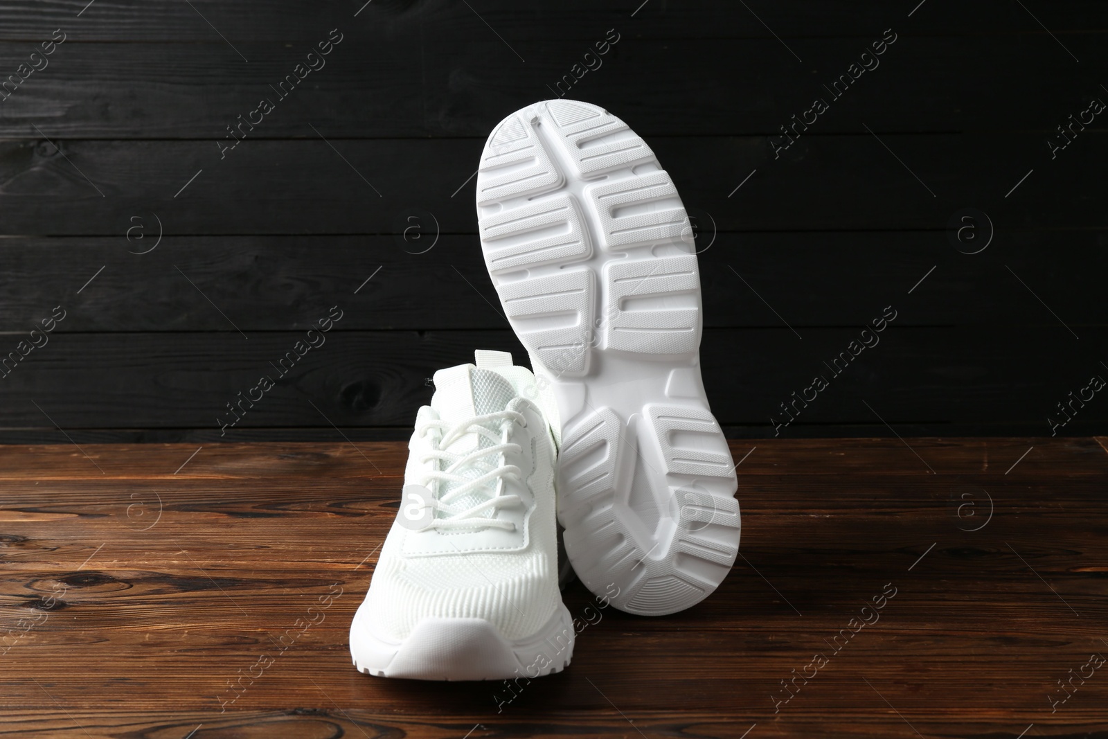 Photo of Pair of stylish white sneakers on floor against dark wooden background