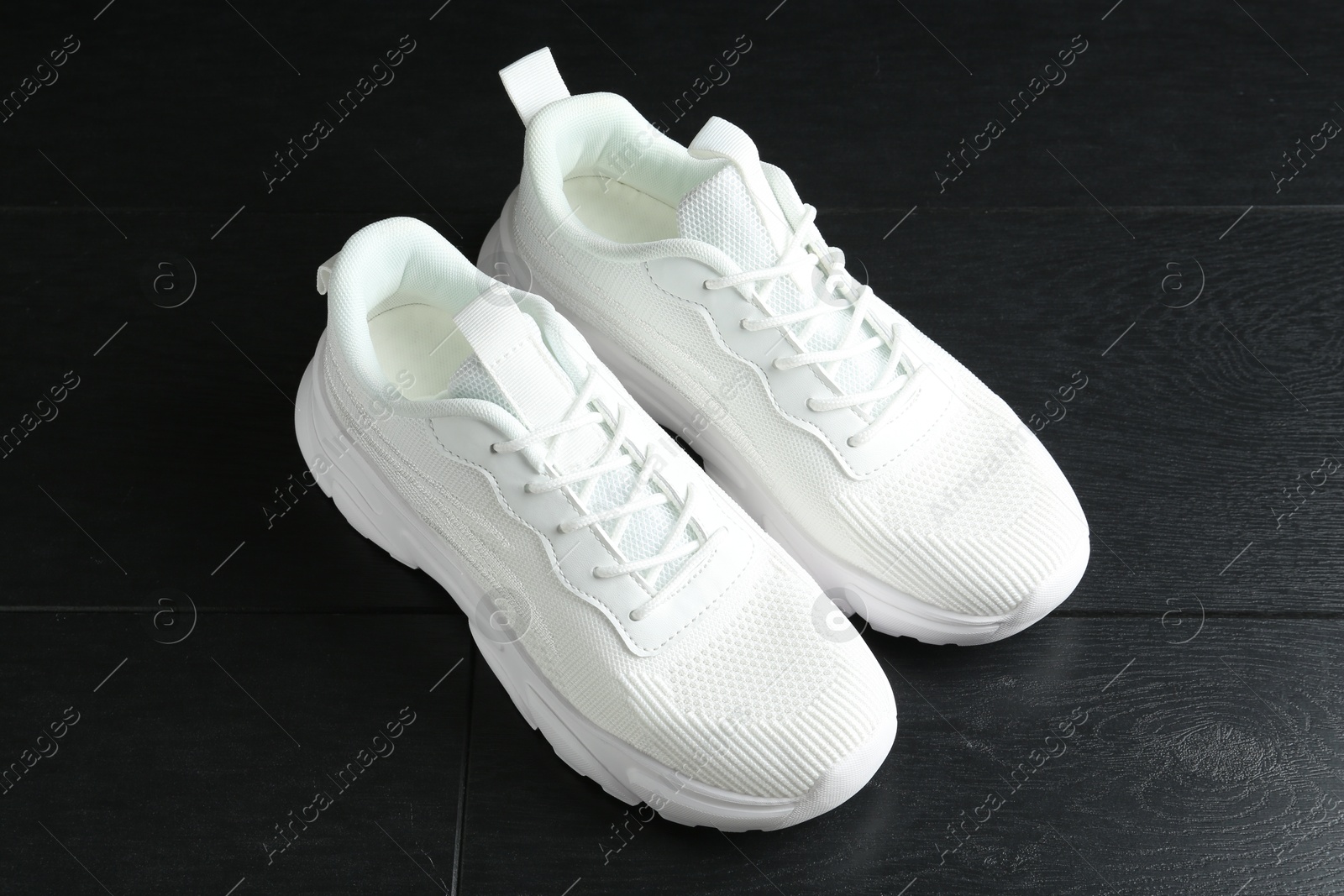 Photo of Pair of stylish white sneakers on black wooden background