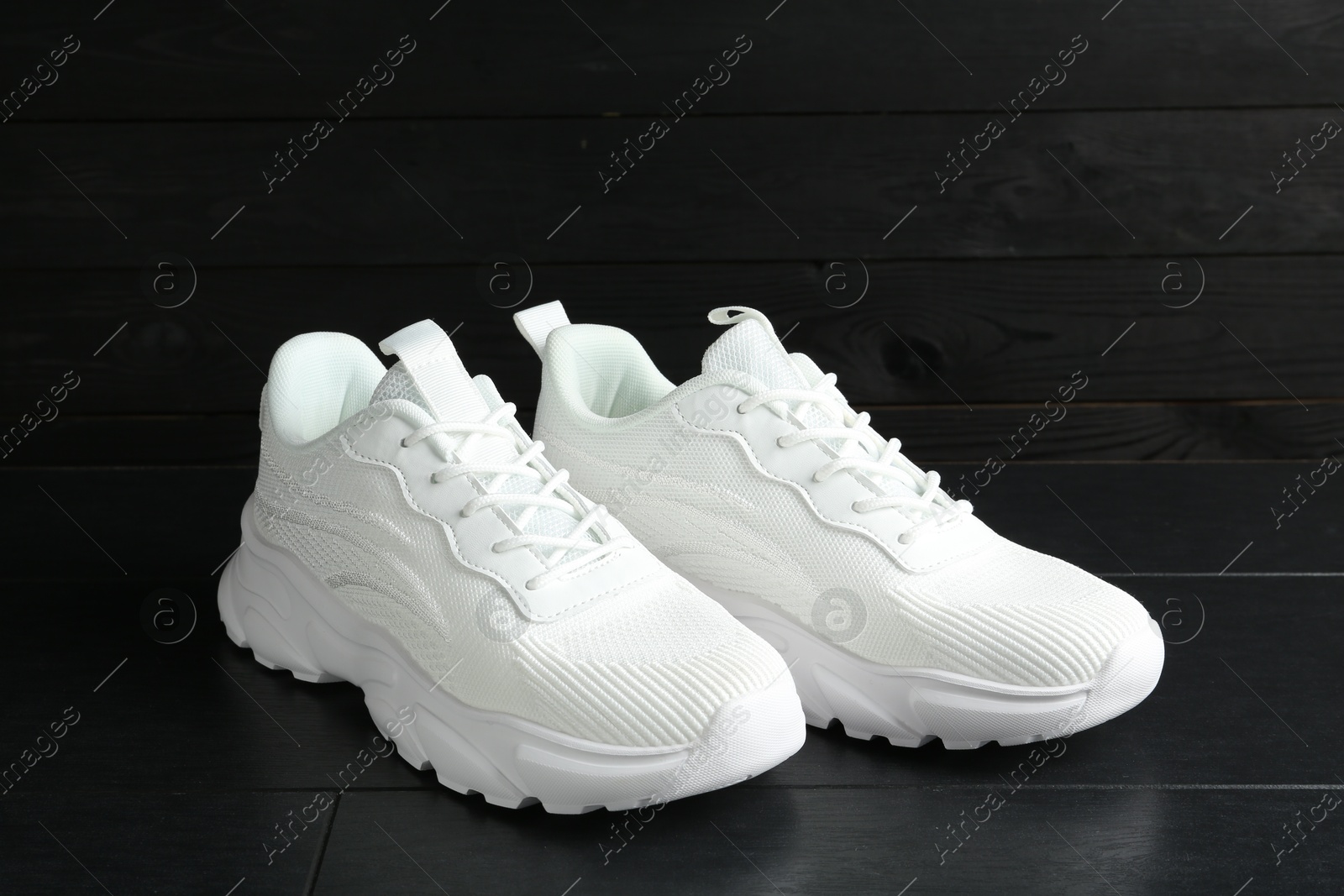 Photo of Pair of stylish white sneakers on black wooden background