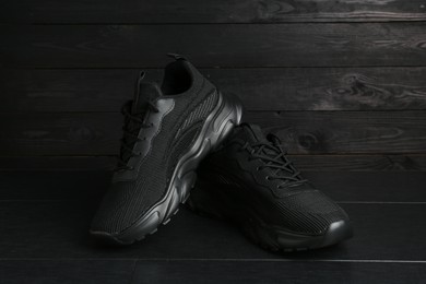 Photo of Pair of stylish black sneakers on dark wooden background