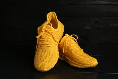 Photo of Pair of stylish yellow sneakers on black wooden background