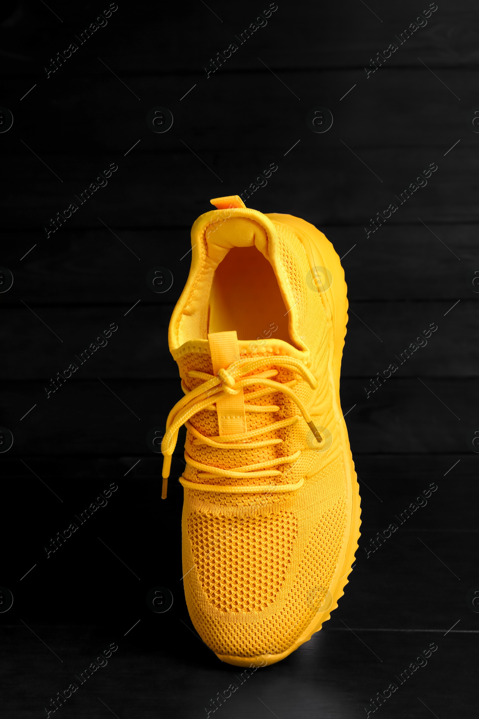 Photo of Stylish yellow sneaker in air on black wooden background