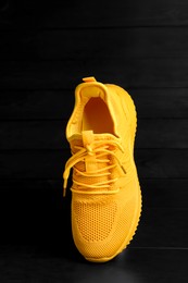 Photo of Stylish yellow sneaker in air on black wooden background