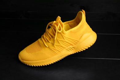 Photo of Stylish yellow sneaker on black wooden background