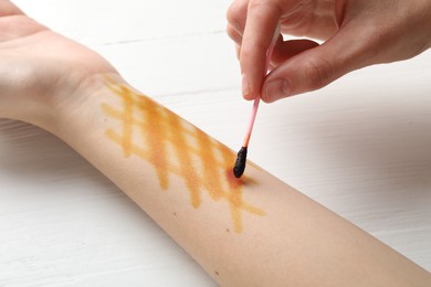 Photo of Woman applying topical iodine with cotton swab on hand at white wooden table, closeup