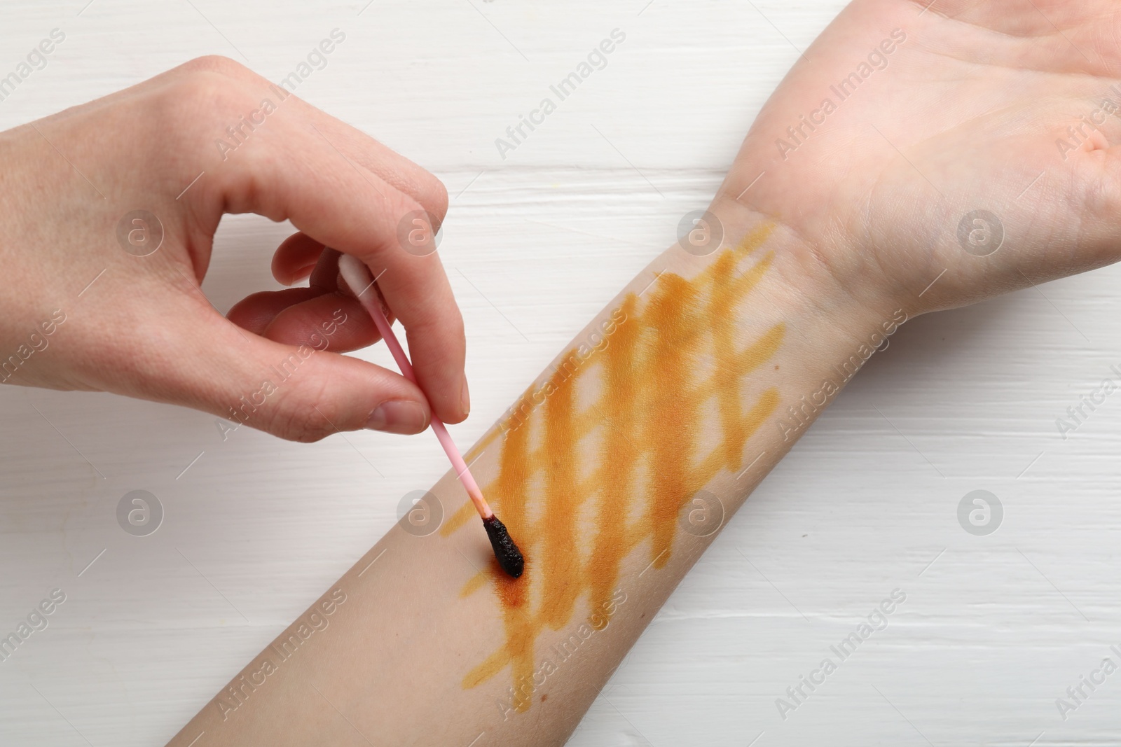 Photo of Woman applying topical iodine with cotton swab on hand at white wooden table, top view