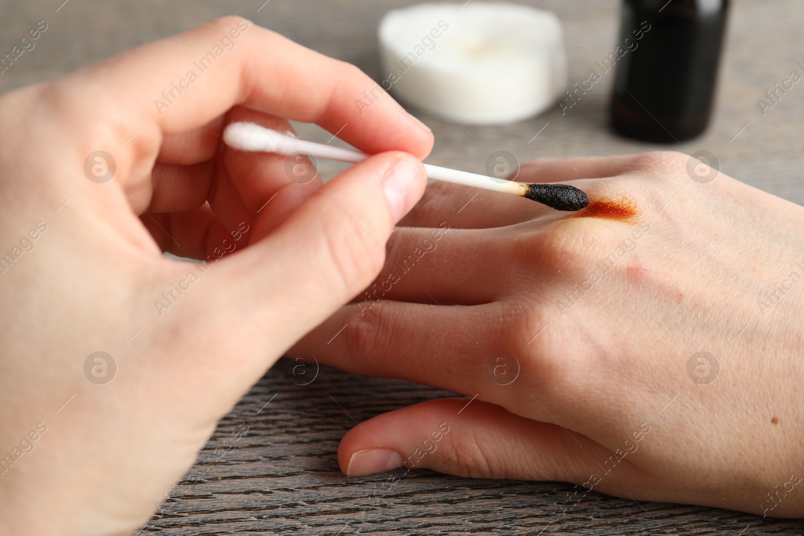 Photo of Woman applying topical iodine with cotton swab on hand at wooden table, closeup